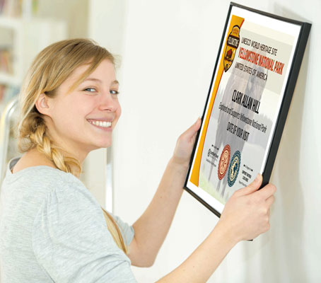 Young woman with blond hair hanging a framed Yellowstone National Park Explorer Certificate on her wall at home